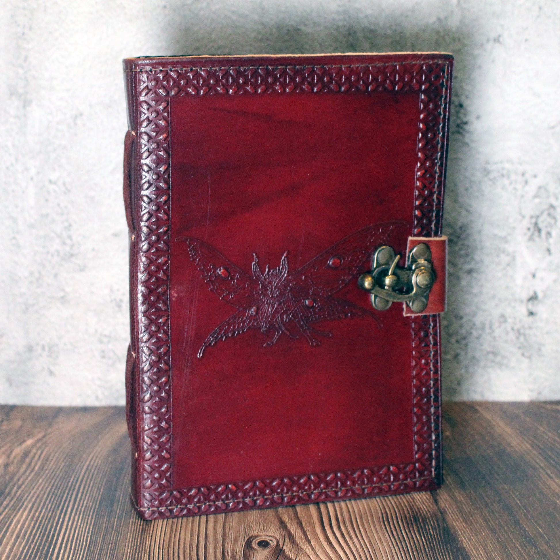 Red leather journal with embossed cryptid design and metal clasp on a wooden surface.