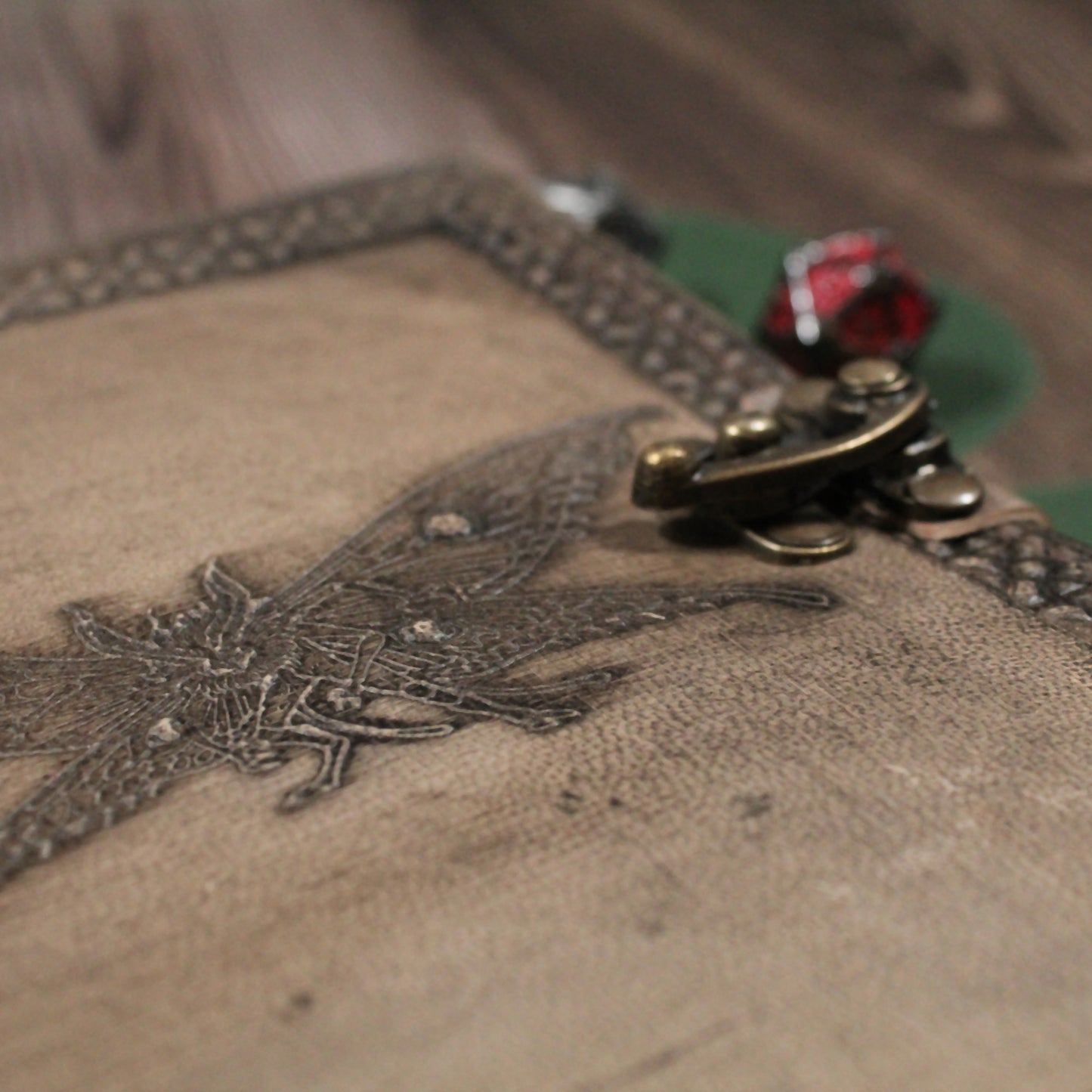 Close-up of a textured surface with an embroidered design of the mothman and a decorative metal clasp.