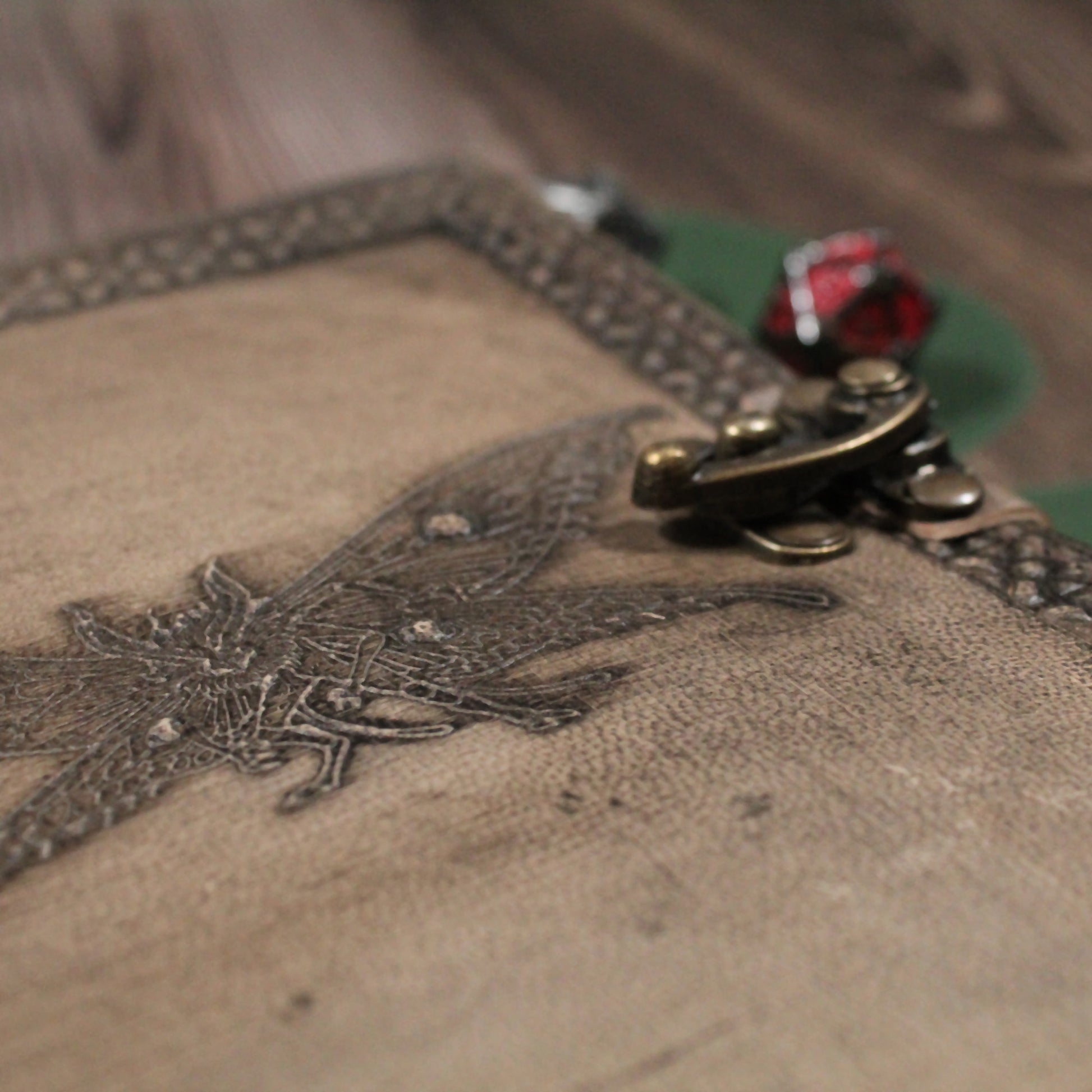 Close-up of a textured surface with an embroidered design of the mothman and a decorative metal clasp.