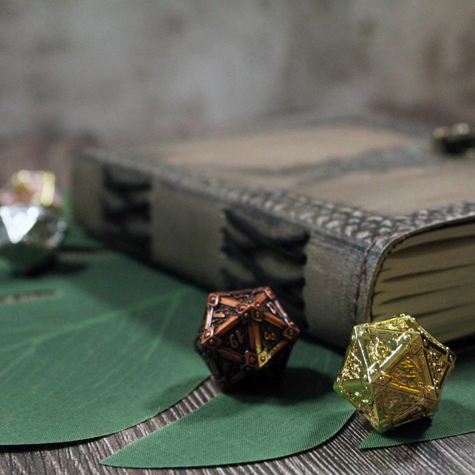 Two metallic dice, one gold and one bronze, on green leaves with a leather journal in the background.
