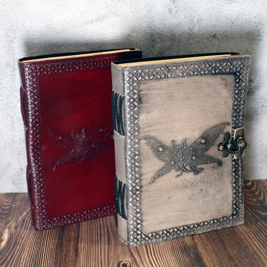 Two ornate leather-bound journals with embossed designs of the cryptid mothman on a wooden surface.