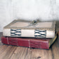 Two books with decorative leather mothman covers stacked on a wooden surface.