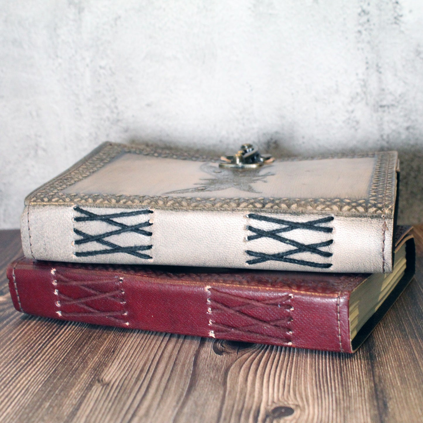 Two books with decorative leather mothman covers stacked on a wooden surface.