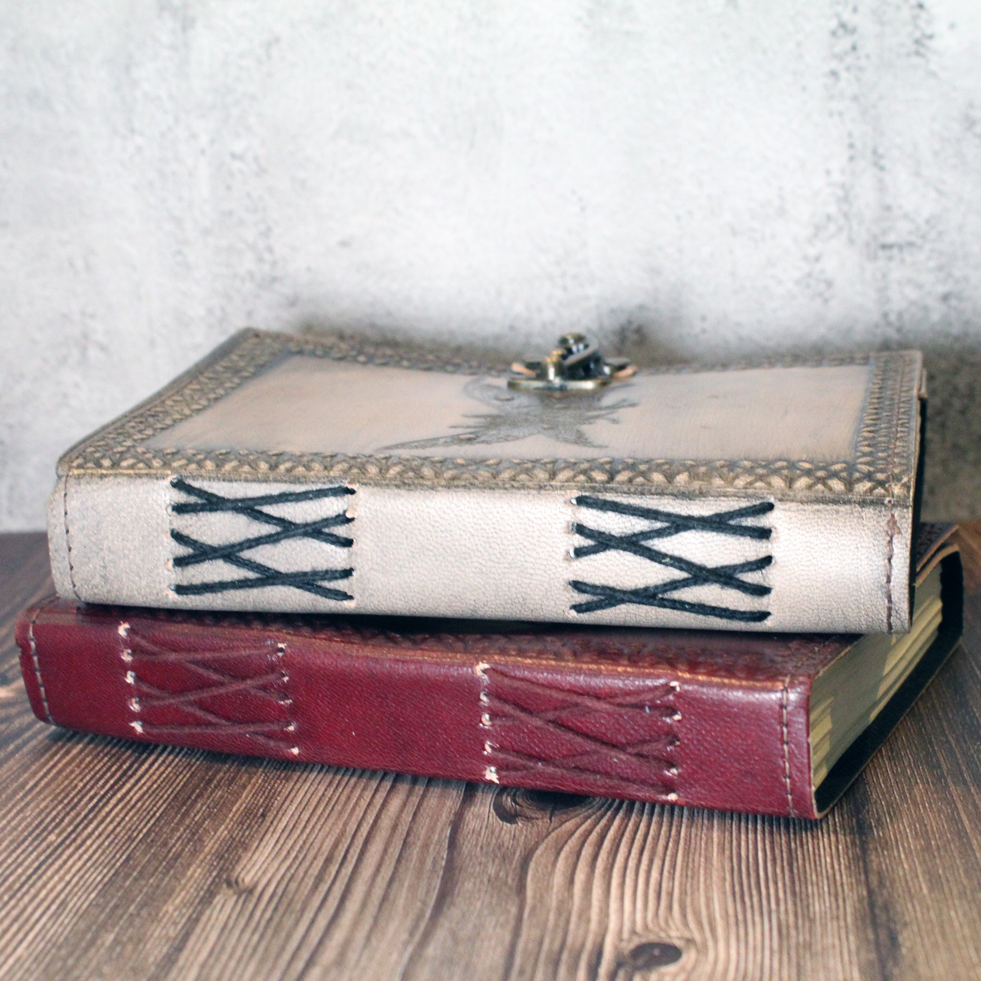 Two books with decorative leather mothman covers stacked on a wooden surface.