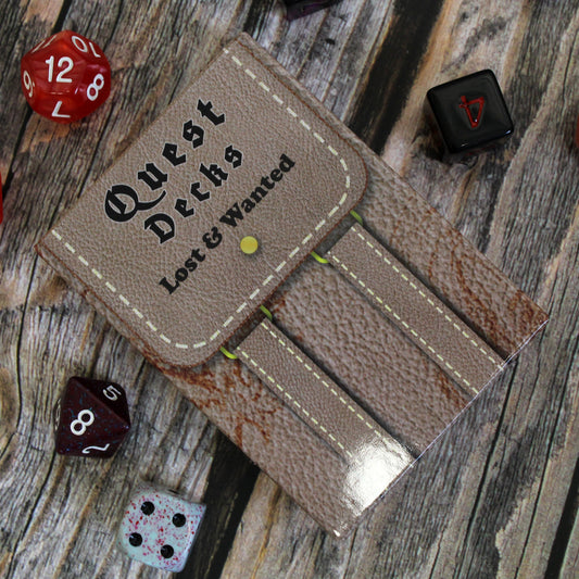 Photo of Quest Deck: Lost & Wanted physical deck box lying face up on a wooden surface with dice scattered around it.  This deck focuses on wanted posters for things like missing people or criminals for adventurers to find.