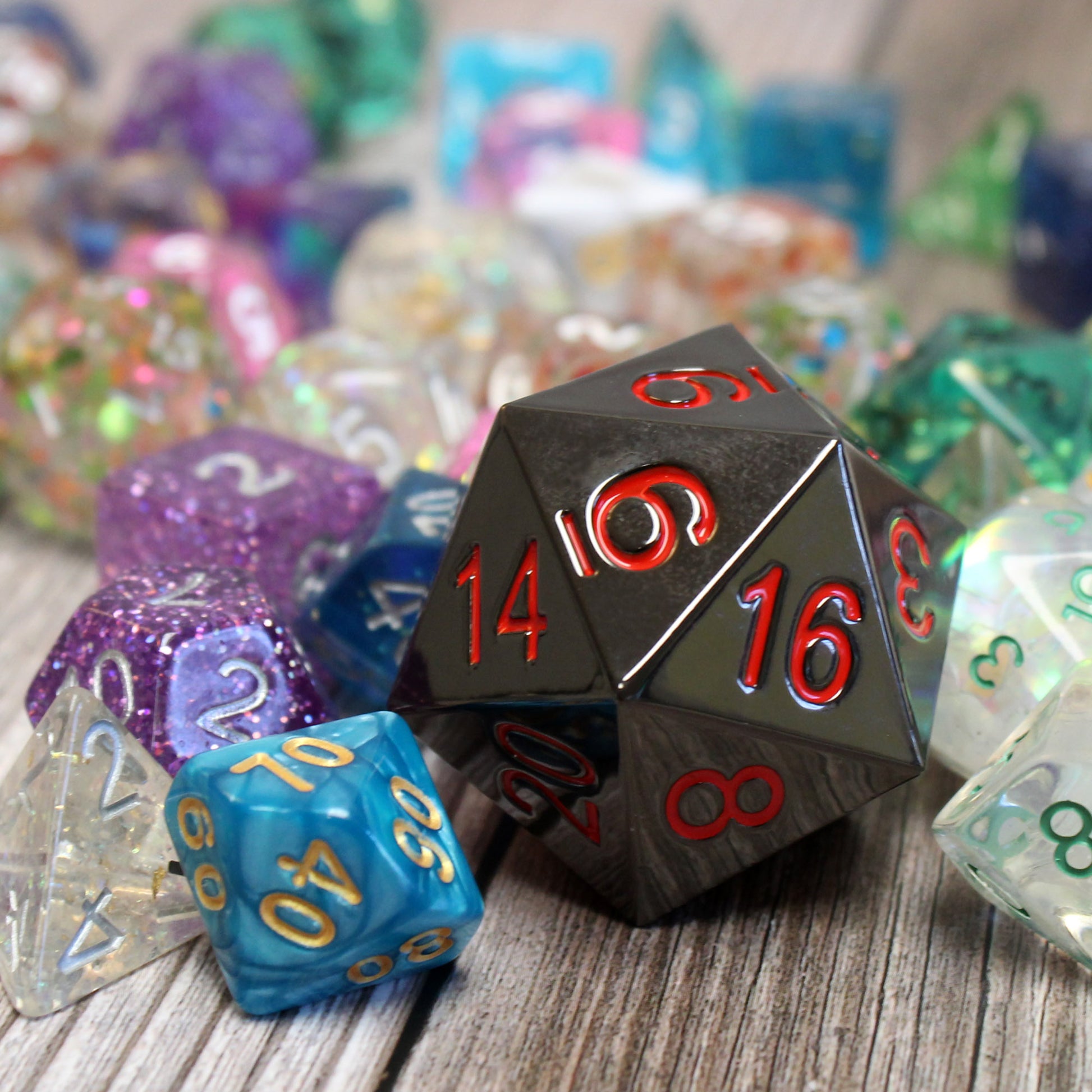 Jumbo Ember 33mm Metal D20 in a Pile of Dice, Showing Off Its Oversized, Hefty Design in Black Electroplated Metal on top of a wooden surface