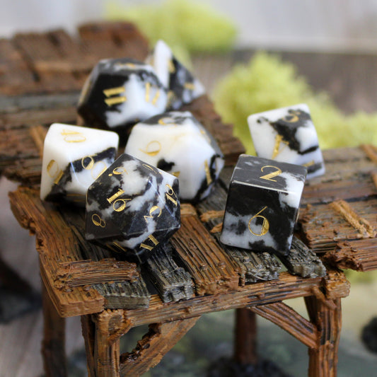 Milk Cow Jasper Gemstone Dice Set displayed on a game table, highlighting the unique black and white pattern and gold font.