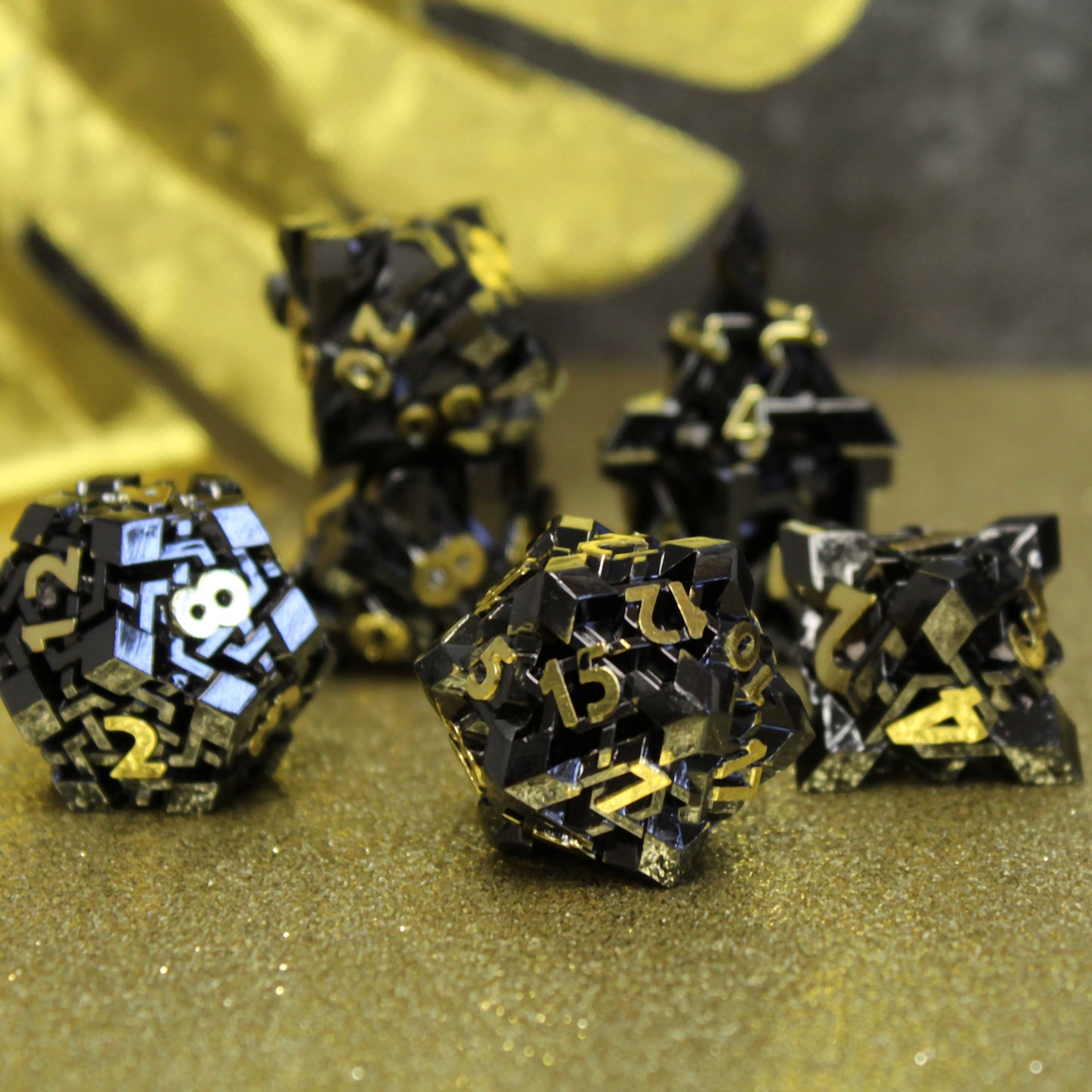 The NightBane dice set arranged in a spread, revealing each die’s elegant, complex pattern and striking contrast between black metal and gleaming gold numbers.