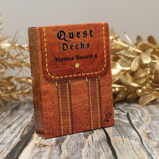 Photo of Quest Deck: Notice Board 2 physical deck box standing upright on a wooden surface with gold plants behind on a white background.  
Notice Board 2 focuses on expanding the quest prompts that fit into any campaign available from the original Notice Board.