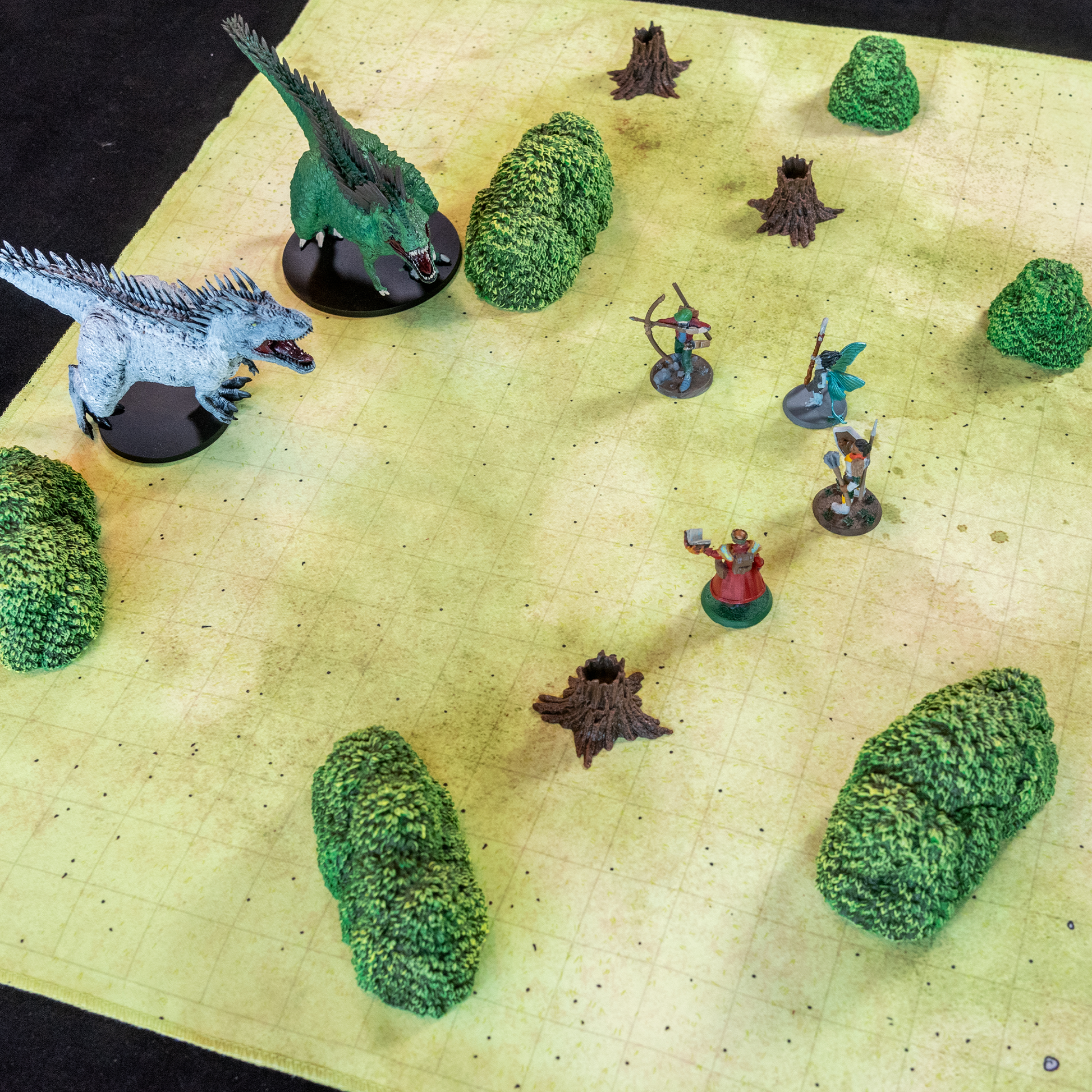Photo of a field battle map with multiple model trees and various miniature figures in a fight scene