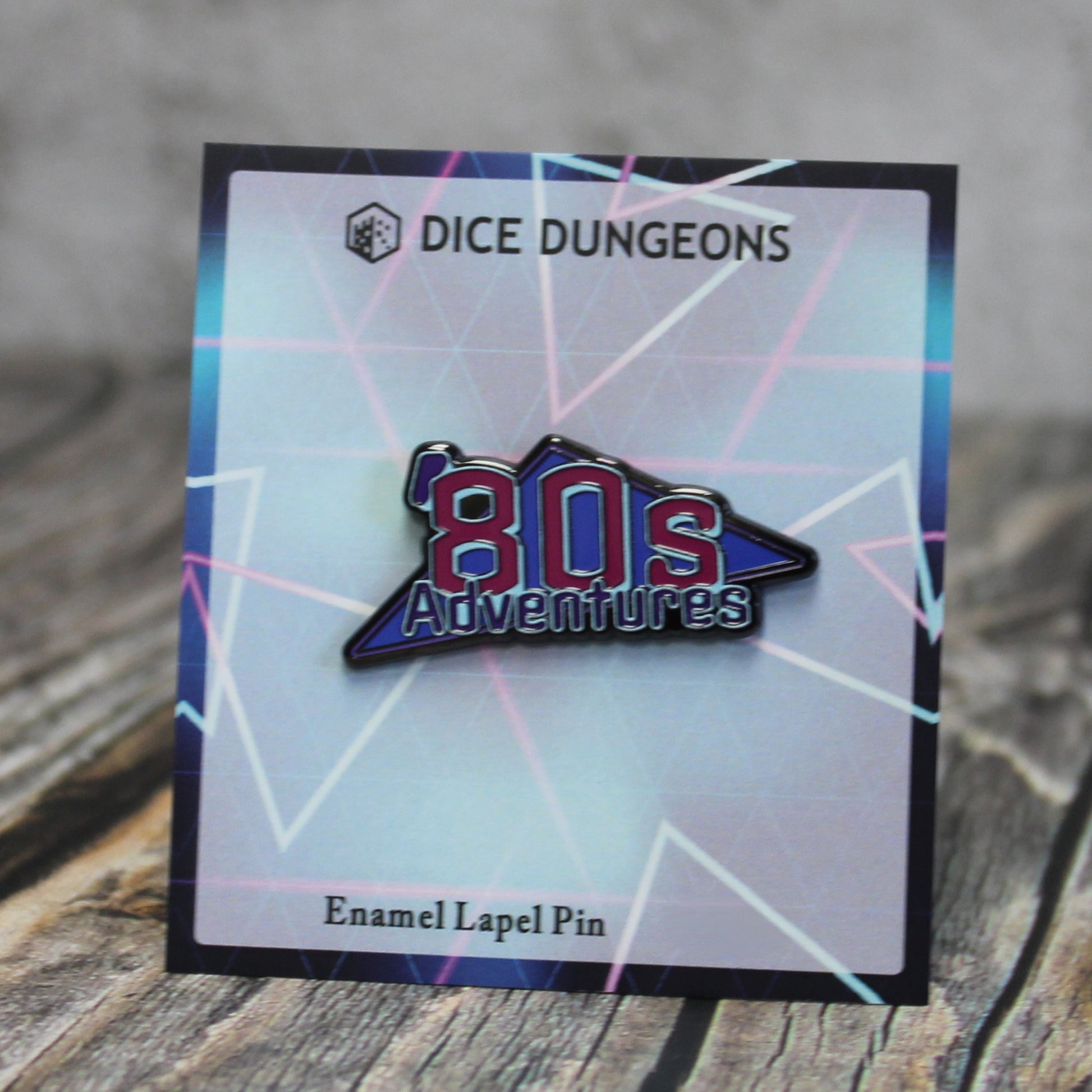 An enamel pin of an "'80s Adventures" logo on a cardboard backing with a geometric neon design