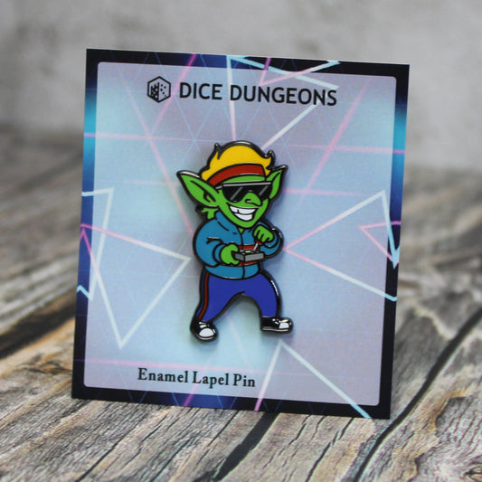 An enamel pin of a goblin wearing 1980s clothing: a red headband, sunglasses, a green jacket, blue trackpants with a red stripe, and sneakers. The goblin is holding a joystick.