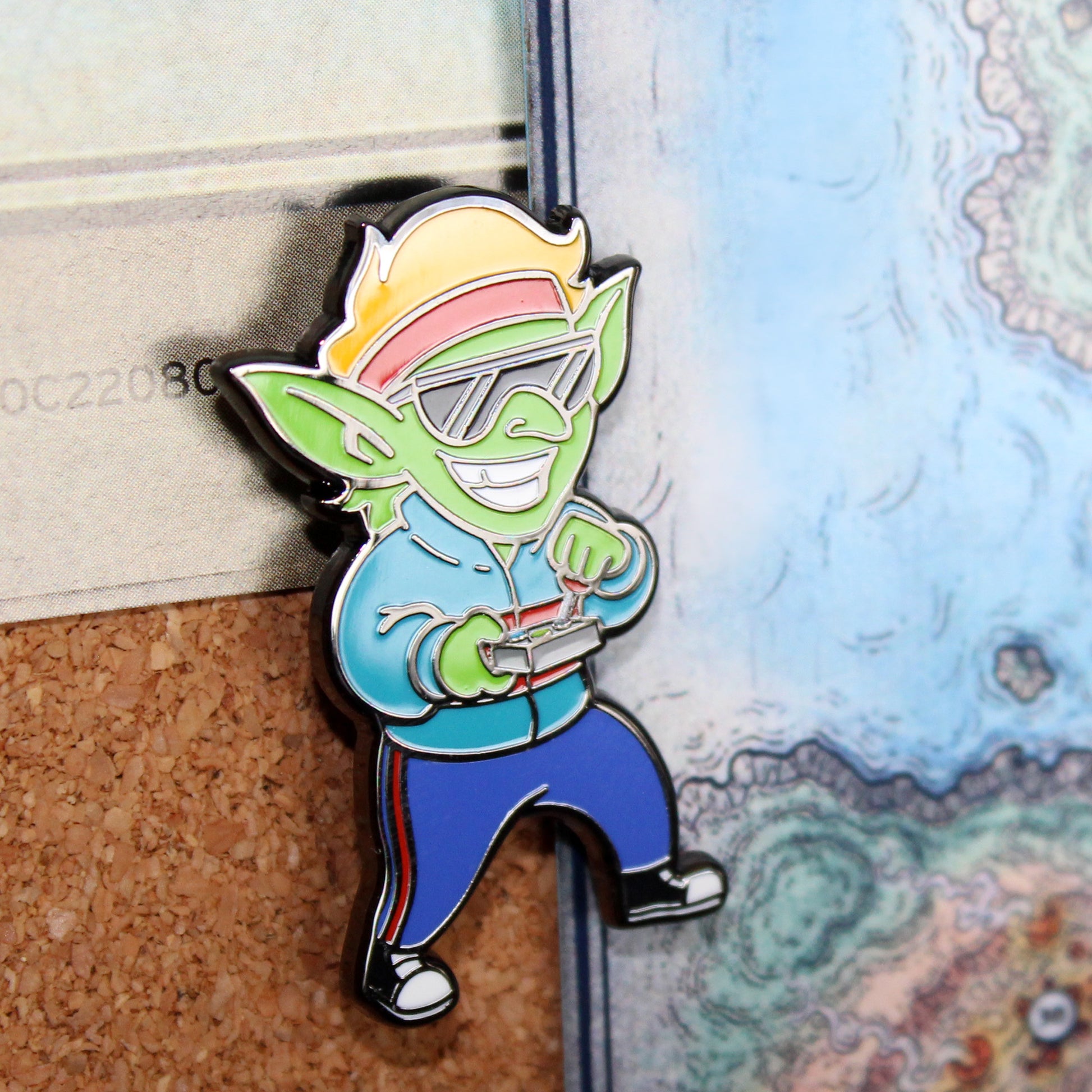 An enamel pin of a goblin wearing '80s clothing pinned to cork board