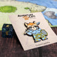 Adventure Cats paladin enamel pin displayed on a tabletop beside a standard d6 die, providing a size comparison.