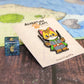 Adventure Cats rogue enamel pin shown on a tabletop next to a standard d6 die, offering a size comparison.