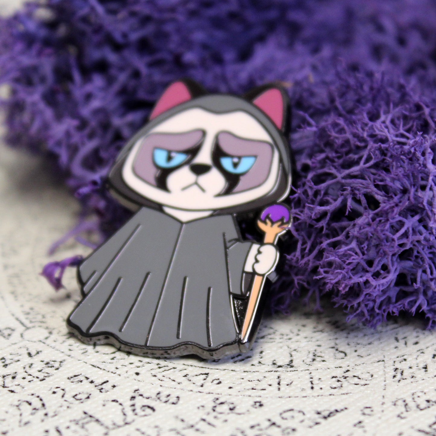 Adventure Cats wizard pin placed in front of purple moss matching the color of the staff.