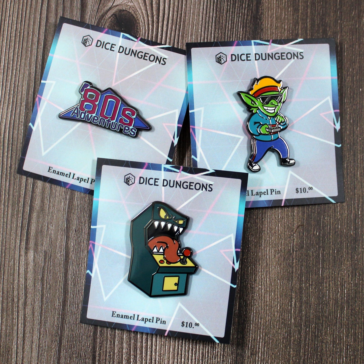 Three enamel pins laying flat on a wooden surface