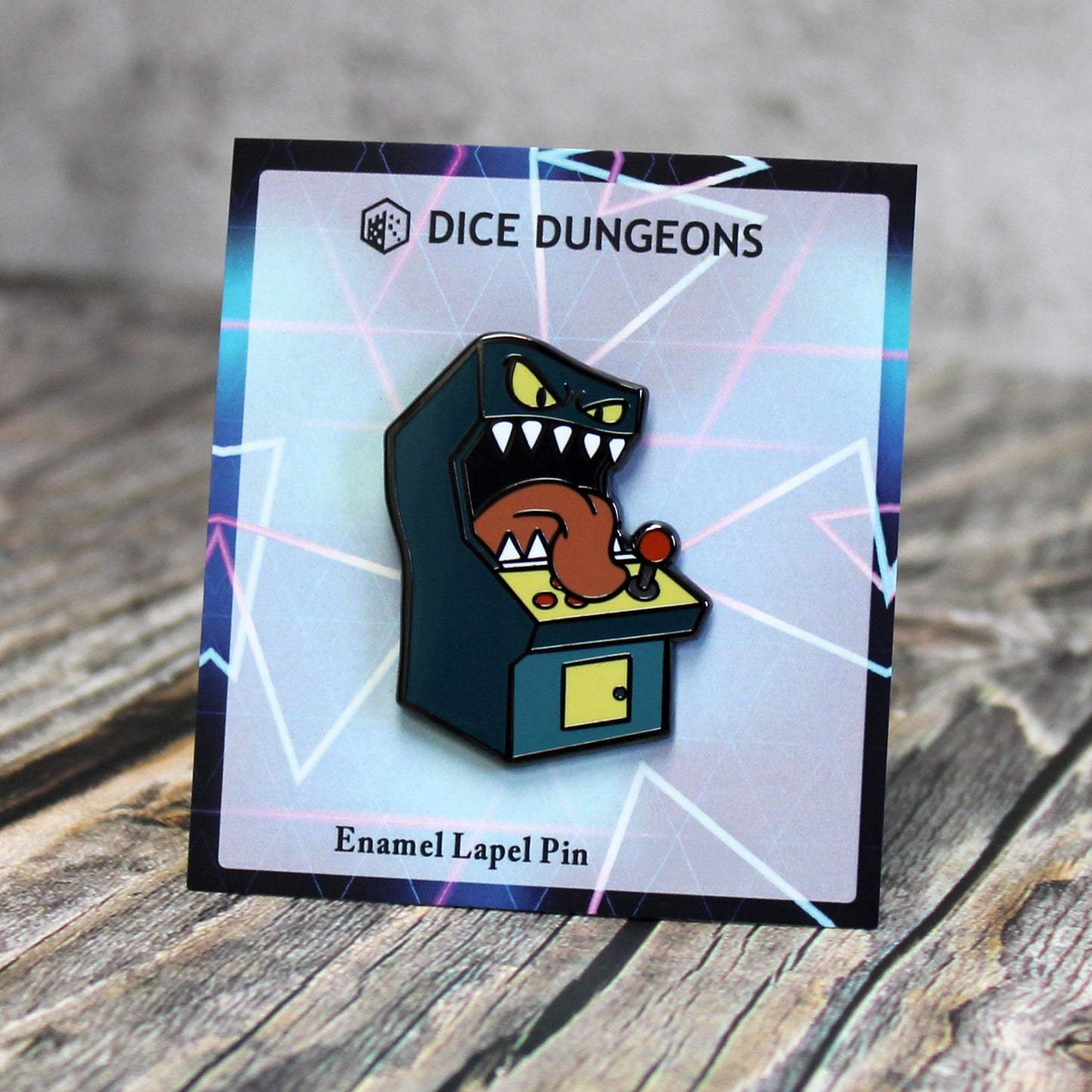 An enamel pin of a standup arcade machine mimic on a cardboard backing with a neon-colored geometric design. 