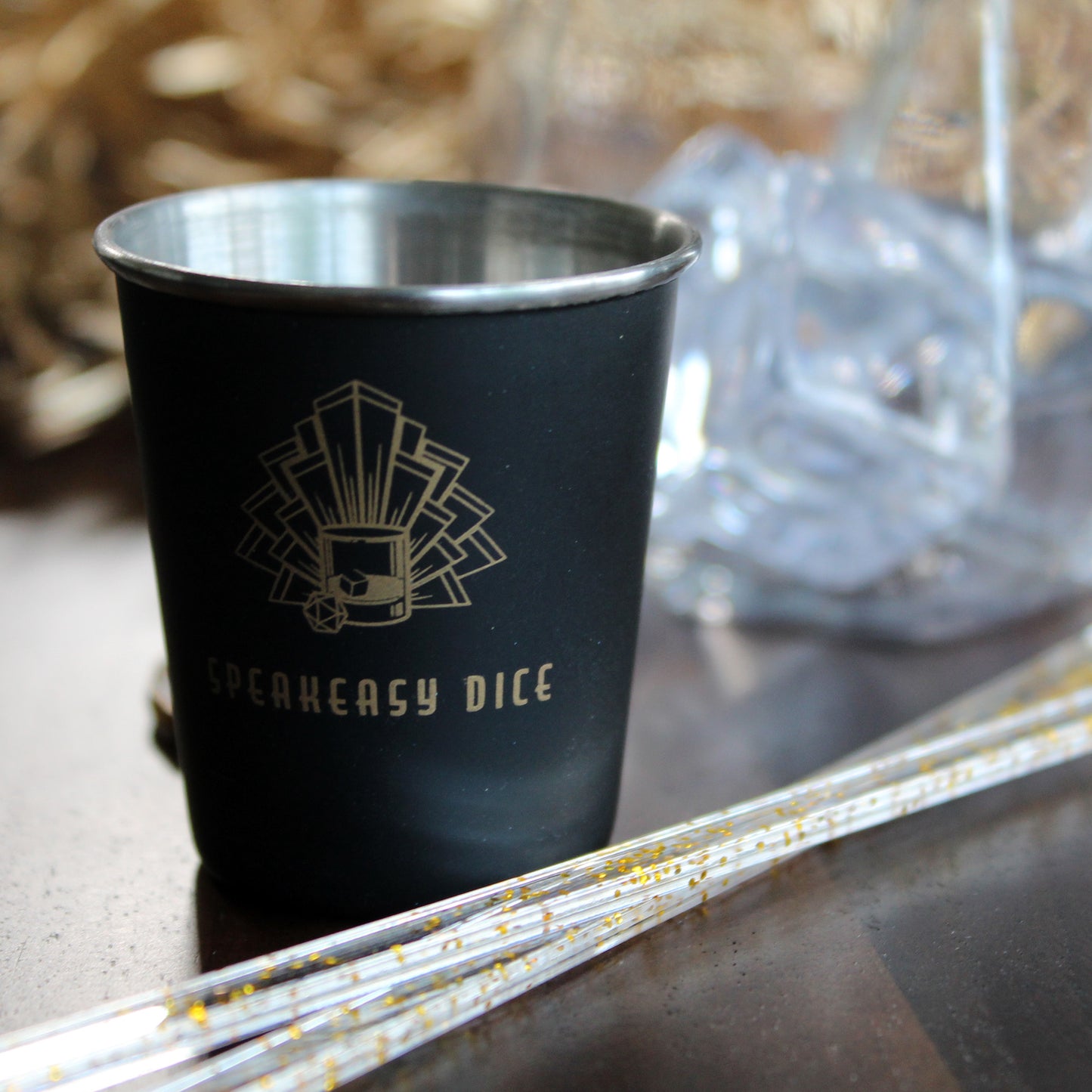 Close-up of the Speakeasy Dice Metal Shot Glass, showcasing its matte black finish and gold Speakeasy Dice logo.