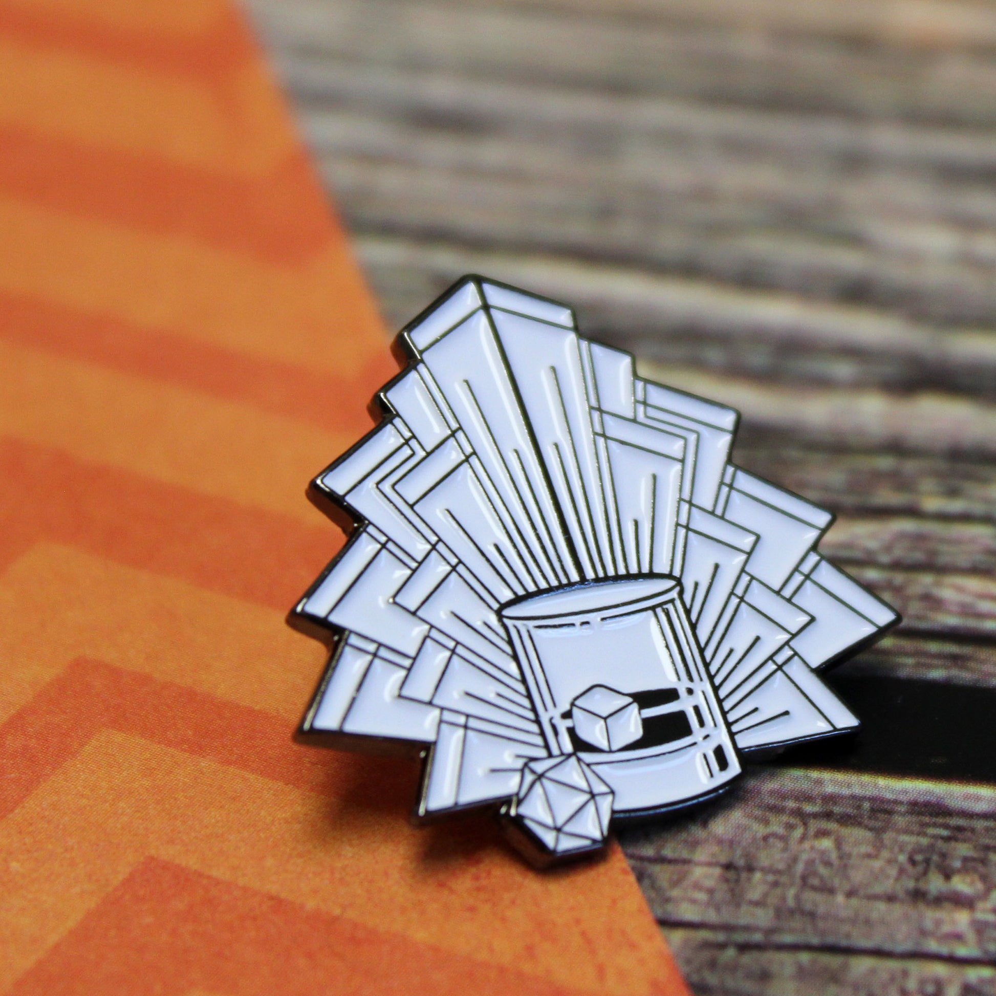 Art deco Speakeasy Dice enamel pin on a tabletop, featuring a dice and cocktail design in white enamel and black nickel-zinc. Perfect for Dungeons & Dragons and TTRPG enthusiasts seeking vintage-inspired gaming accessories.