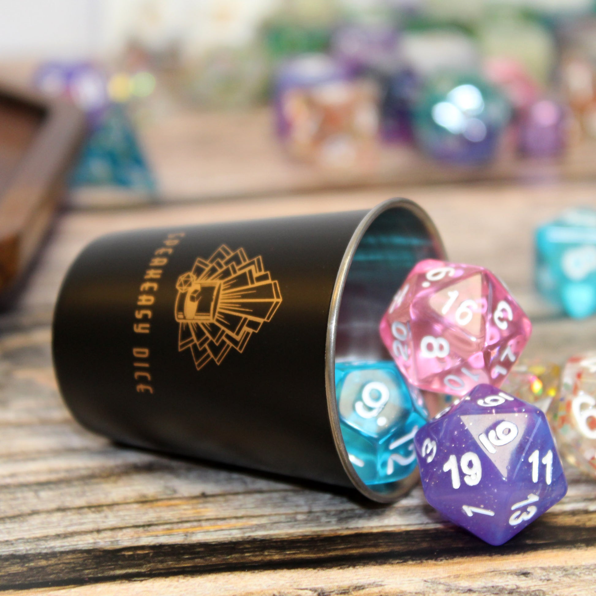 Metal Shot Glass tipped on its side with RPG dice spilling out, highlighting the matte black exterior and golden logo. A stylish gaming accessory for TTRPG players.