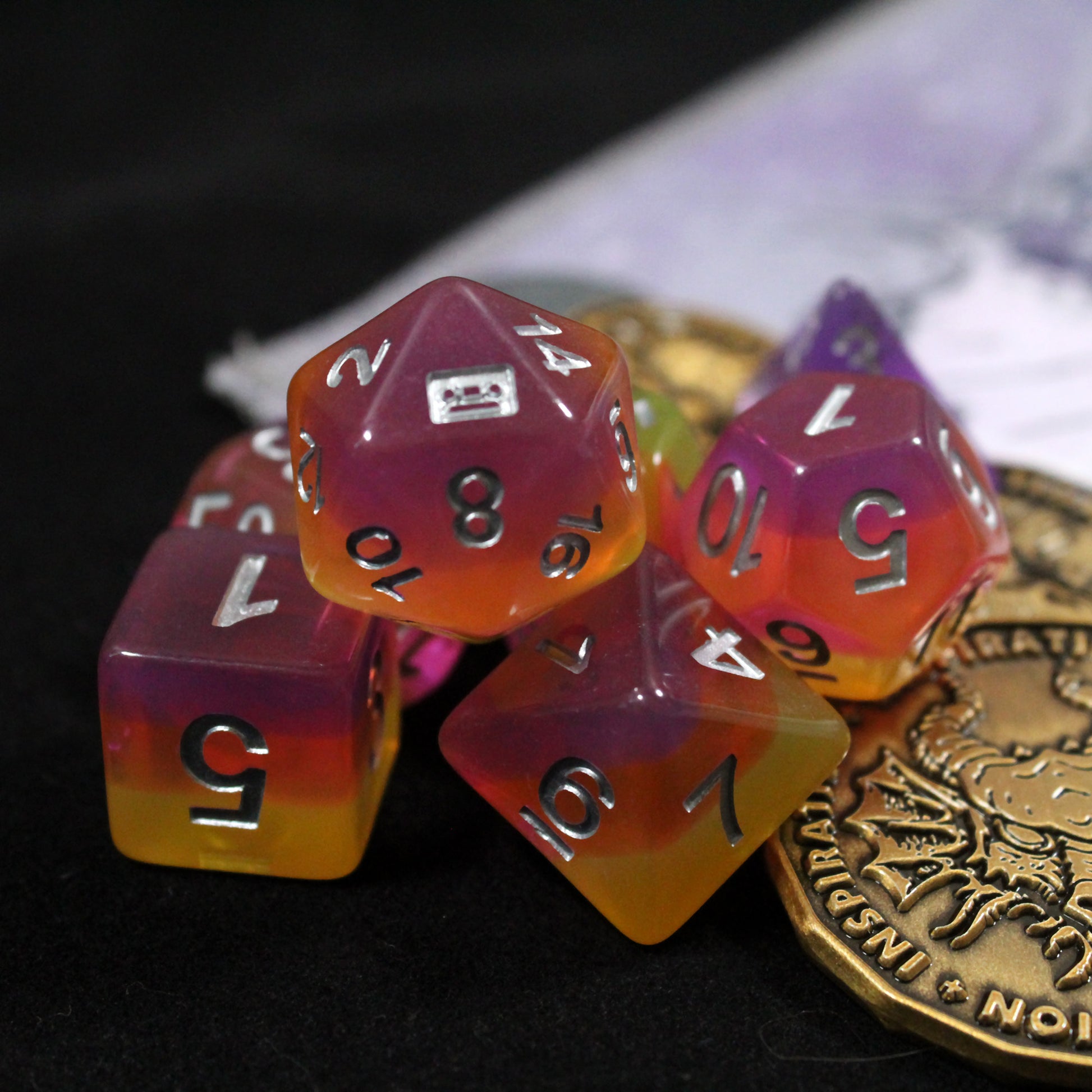Set of pink and orange polyhedral dice with some golden tokens on a play mat