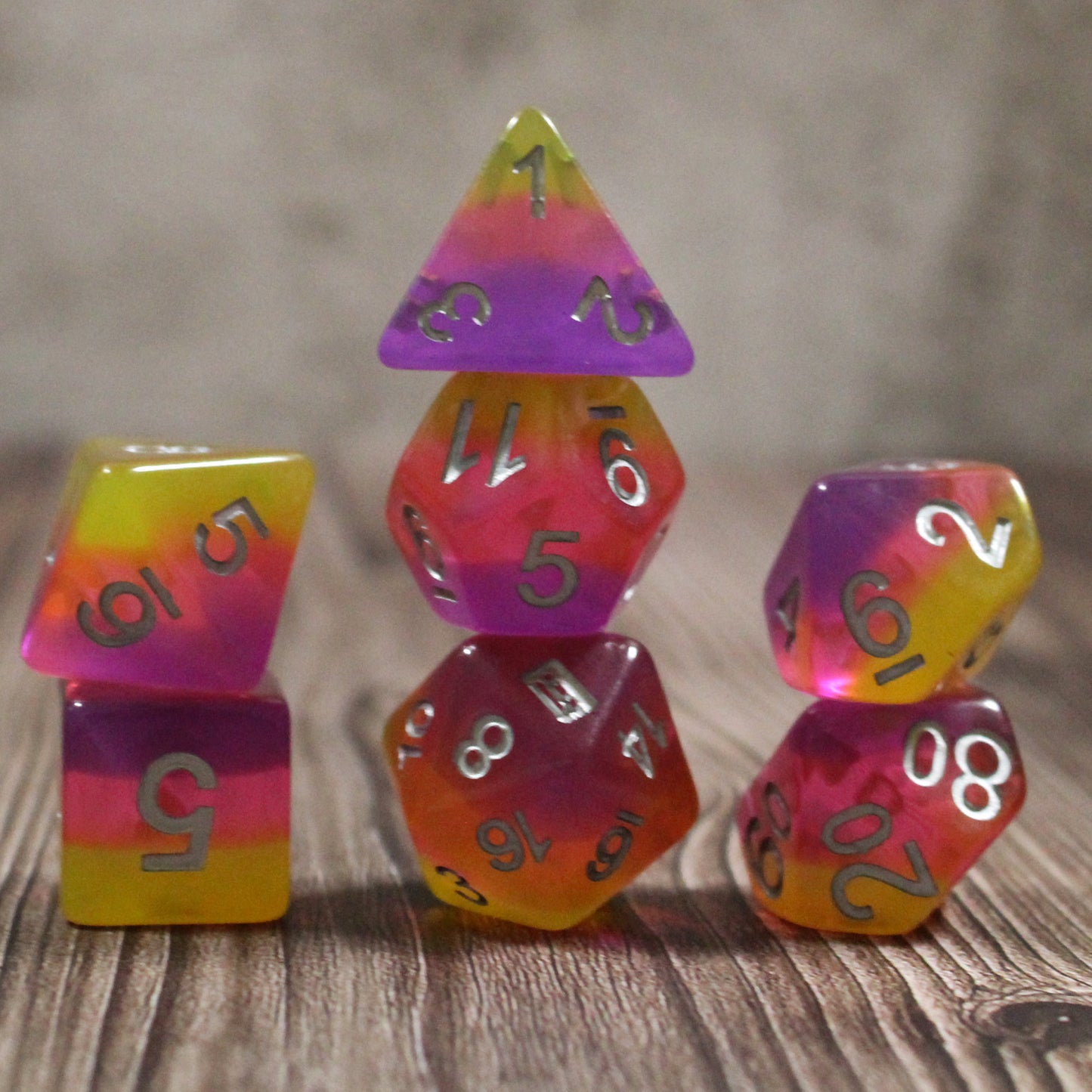 Set of pink and orange polyhedral dice neatly stacked on a wooden surface