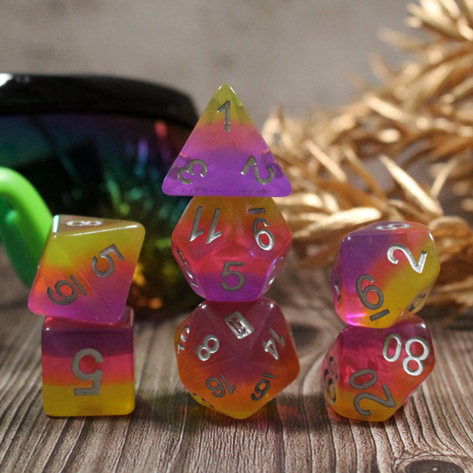 Set of pink and orange polyhedral dice on a wooden surface with sunglasses and golden leaves in the background