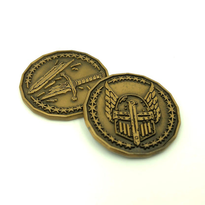 Dice Dungeons' Paladin Character Coin in an antique gold finish front and back on a white surface.  The front face overlaps the back face and has a winged helmet encircled by stars while the back face has a broken sword surrounded by the same ring of stars. 