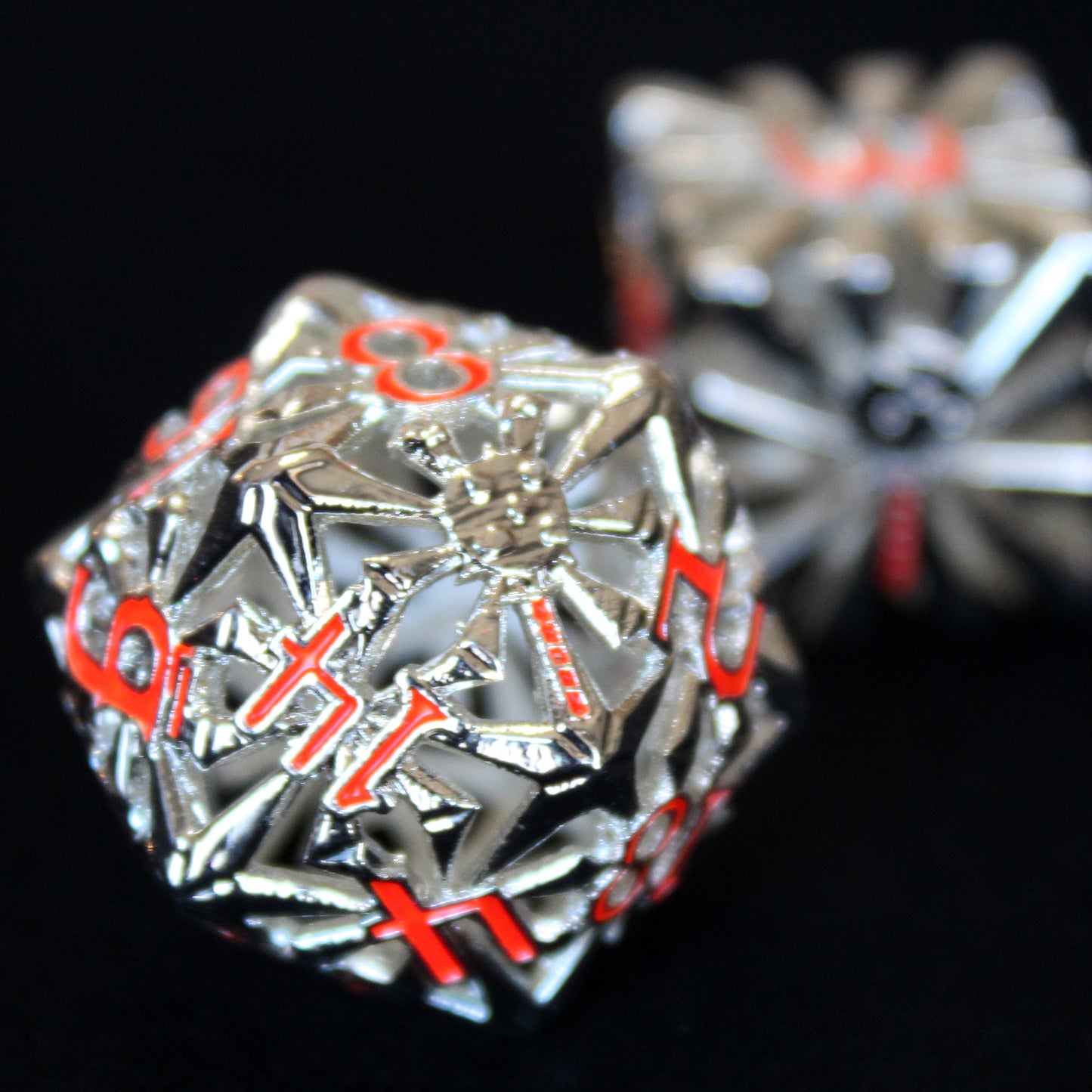 Closeup of bright silver cleric-inspired hollow metal dice with red numbering and a mace in place of the high number on a black backgrond