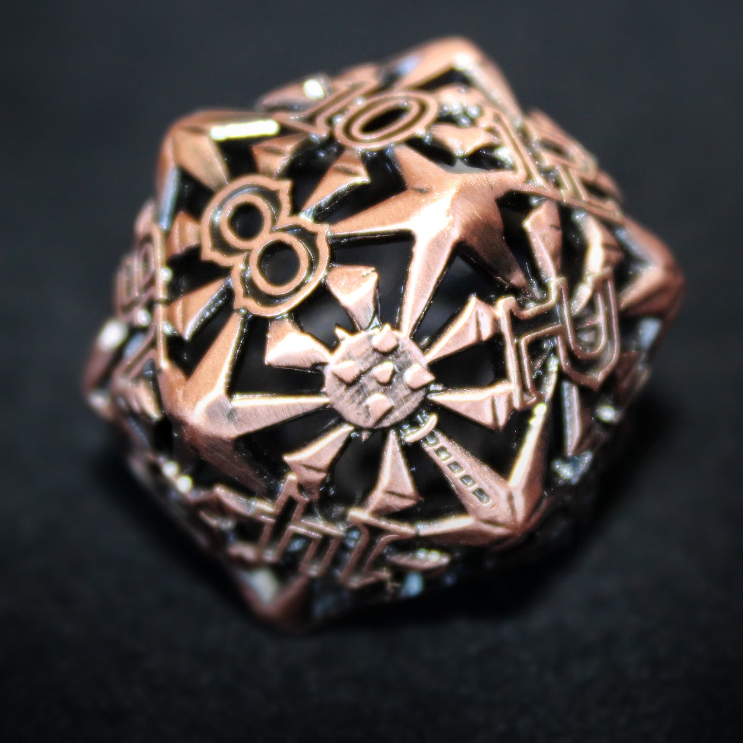 Closeup of a copper-colored cleric-inspired hollow metal twenty-sided die with uninked numbers and a mace in place of the high number