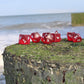 A set of red translucent glass RPG dice with silver numbering on a small grassy model cliff