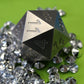 An oversized silver-colored metal twenty-sided die sitting on a pile of rhinestones on a green background.