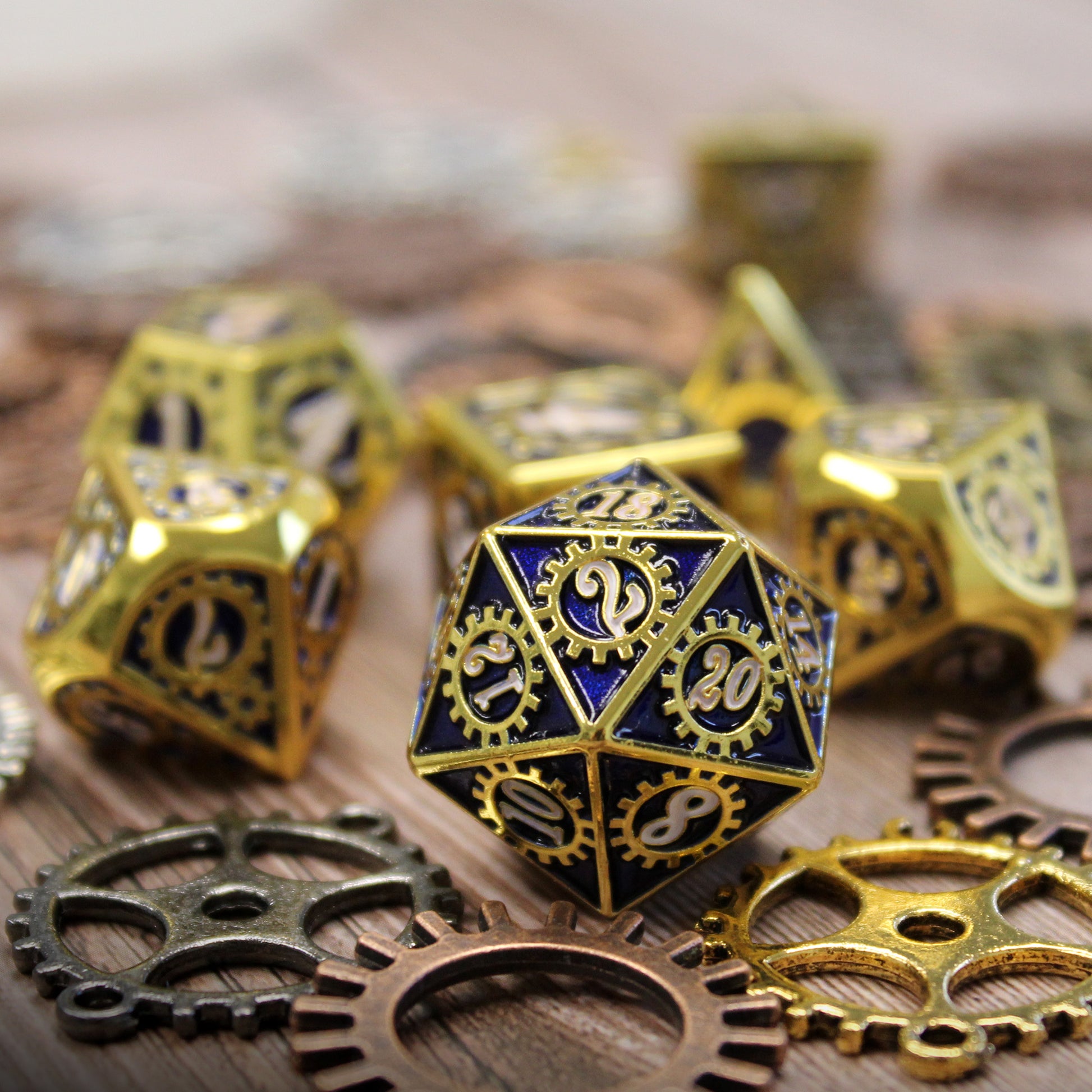 Detail view of the Mechanist Bule and Gold set d20 with the 2 face towards the viewer resting on a wooden surface with decorative gears and cogs in the foreground and the remainder of the dice set out of focus in the background.