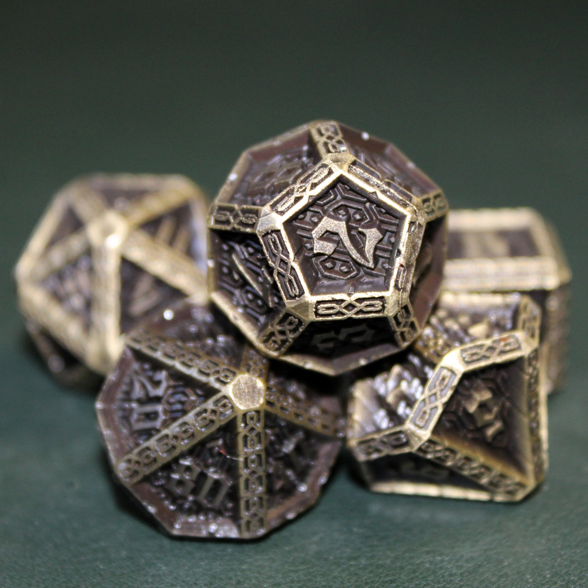 Close up detail shot of the d12 on the 2 face of the Cavalier Bronze set, other die from the set are beneath and out of focus on a dark green surface.