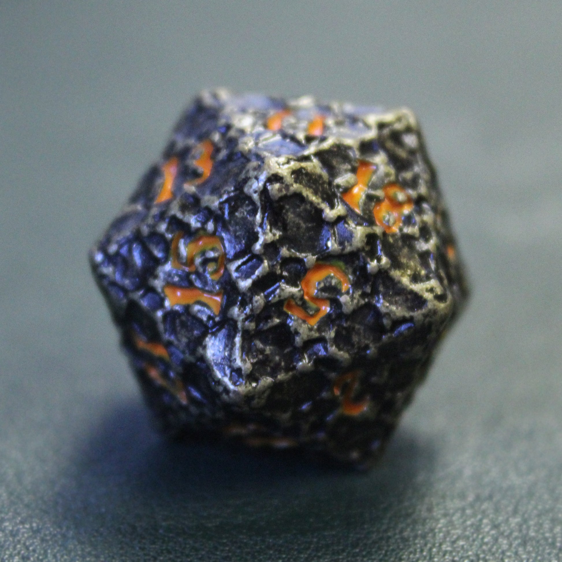 Closeup detail picture of the Geomancer Black dice set's d20 on a dark green surface with the 5 face towards the viewer.