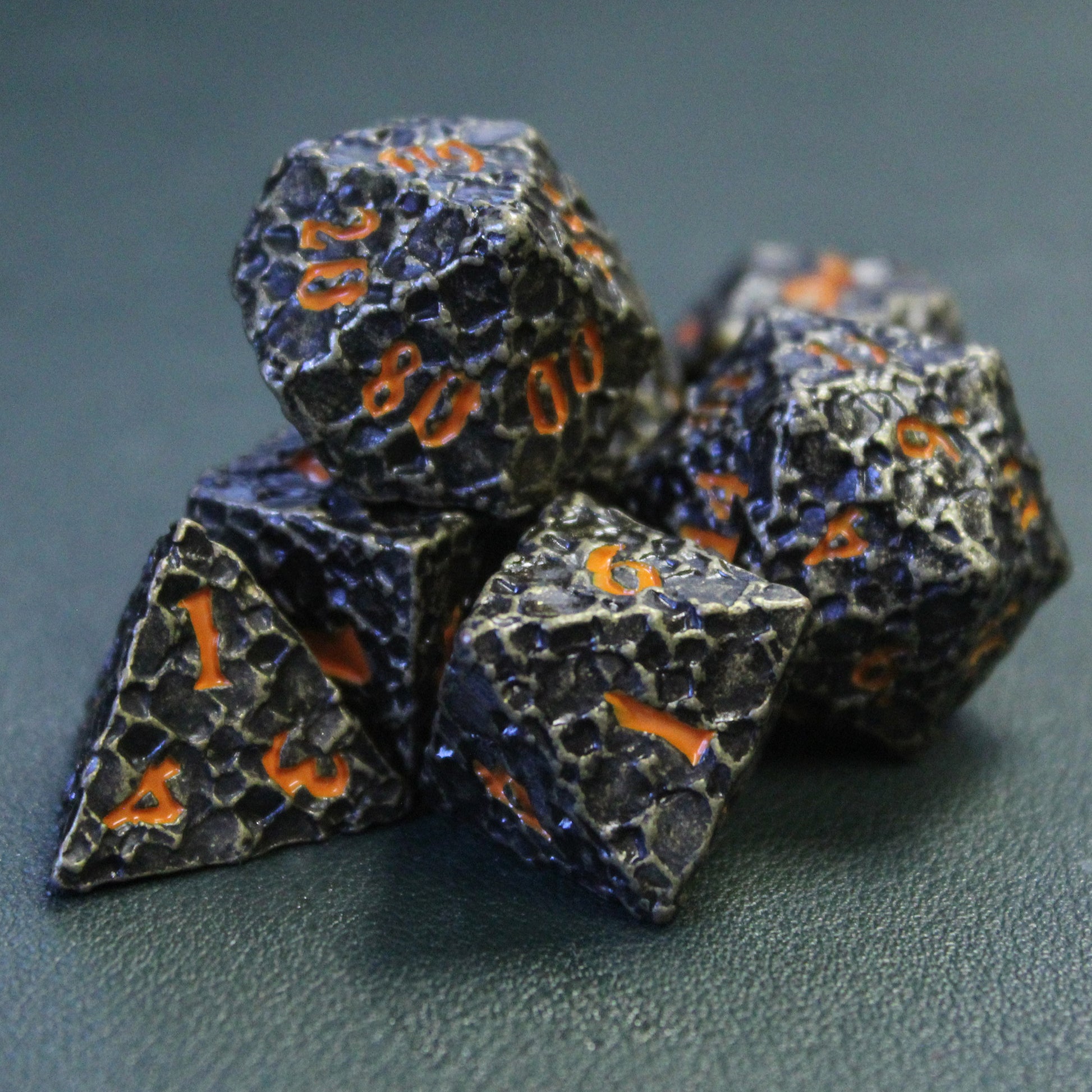 Geomancer Black dice set on a faux leather surface with the d8 in the foreground.  Each die has a worn metal finish with a bronze color visible through the finish on the raised surfaces.