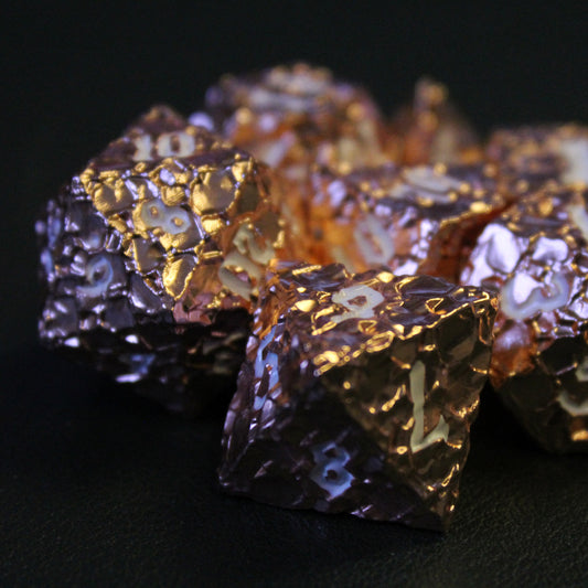 Close up shot of the Geomancer Copper dice set on a black surface.  Each die is primarily copper in color with white numbering.  The copper portion has a beaten metal finish.