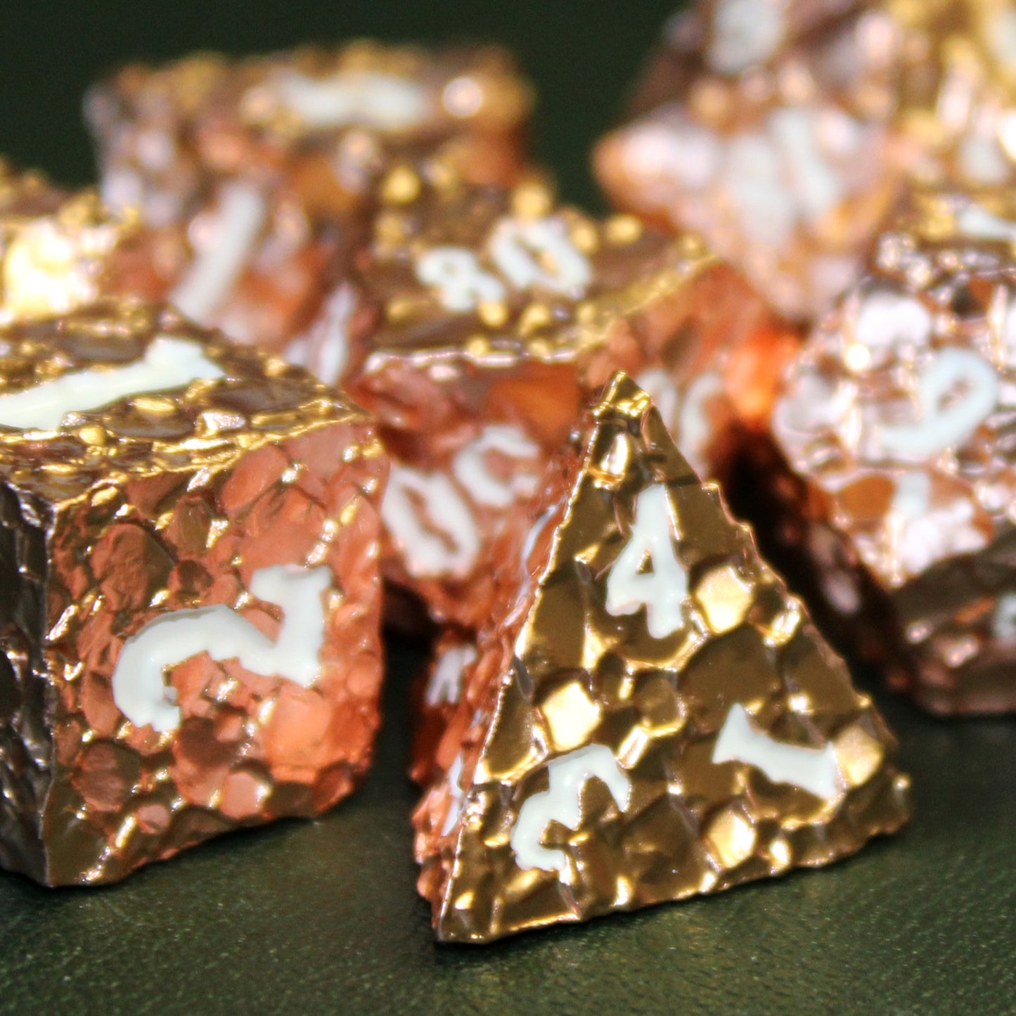 Close up image of the Geomancer Copper dice set with the d6 and d4 in focus in the foreground on a dark green surface.  Other dice from the set are out of focus and frame in the background.