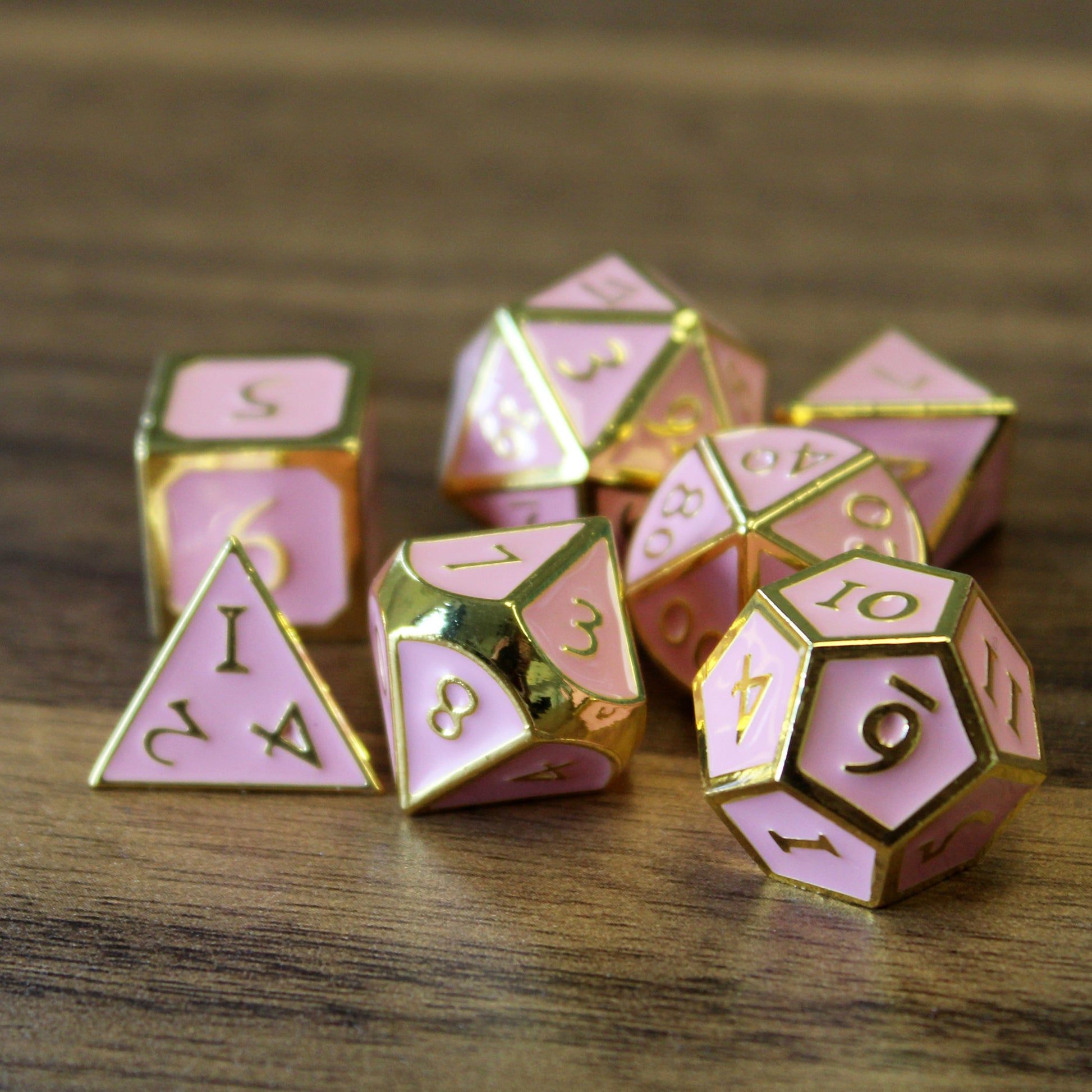 Metal Imperial Pink dice set arranged in a pile on a wood surface. 