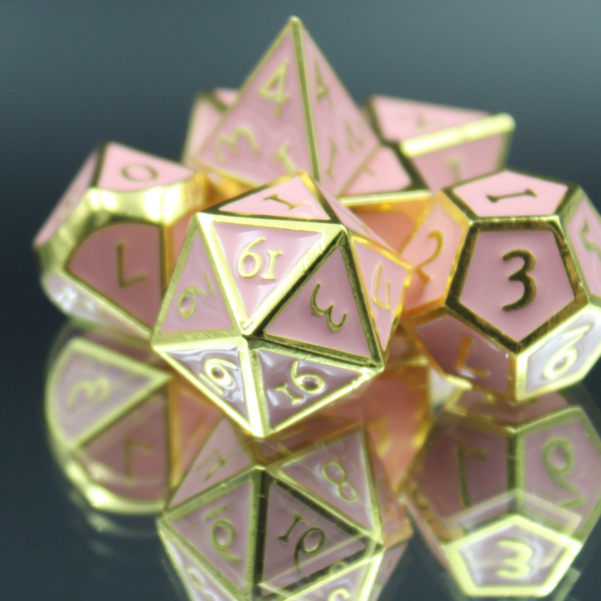 Metal Imperial Pink Dice set arranged in a pile on a reflective surface with the D20 and D12 in front. The dice have gold edging and numbers with light pink on each side. 