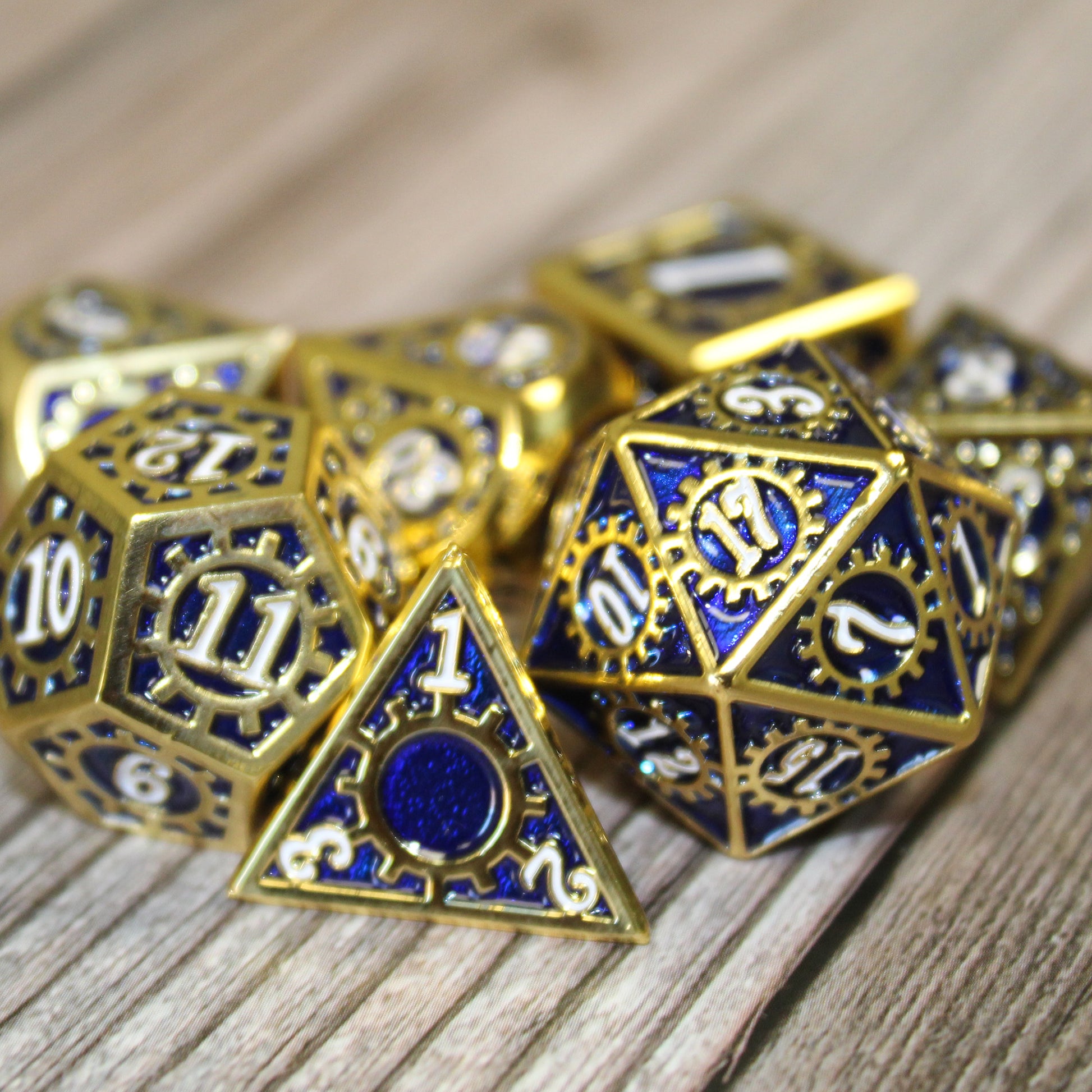 Blue and Gold Mechanist Metal RPG dice set resting on a wooden surface with the d4, d12, and d20 in the foreground.