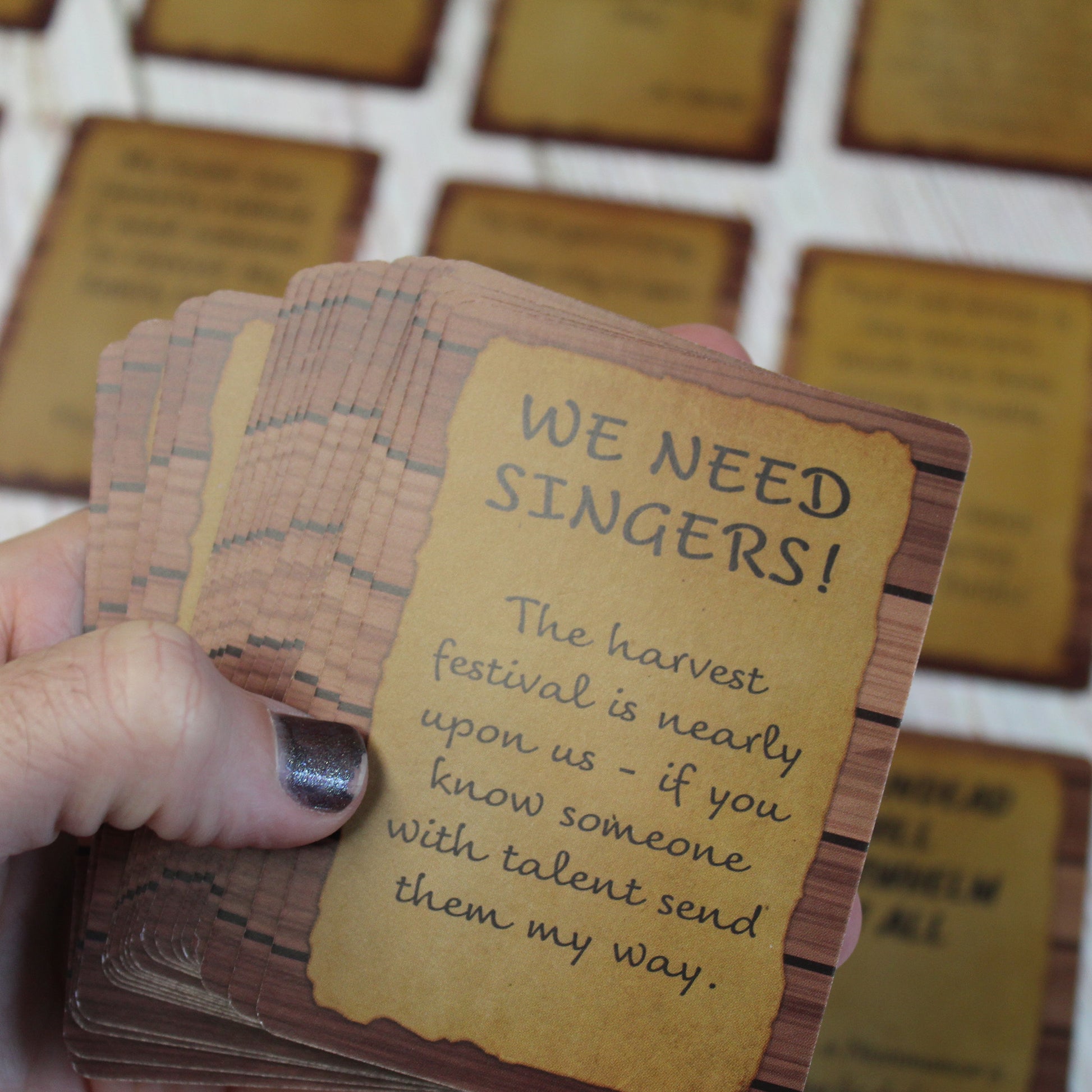 Hand holding several cards from The Notice Board quest deck. The main card show a need for singers at the harvest festival.