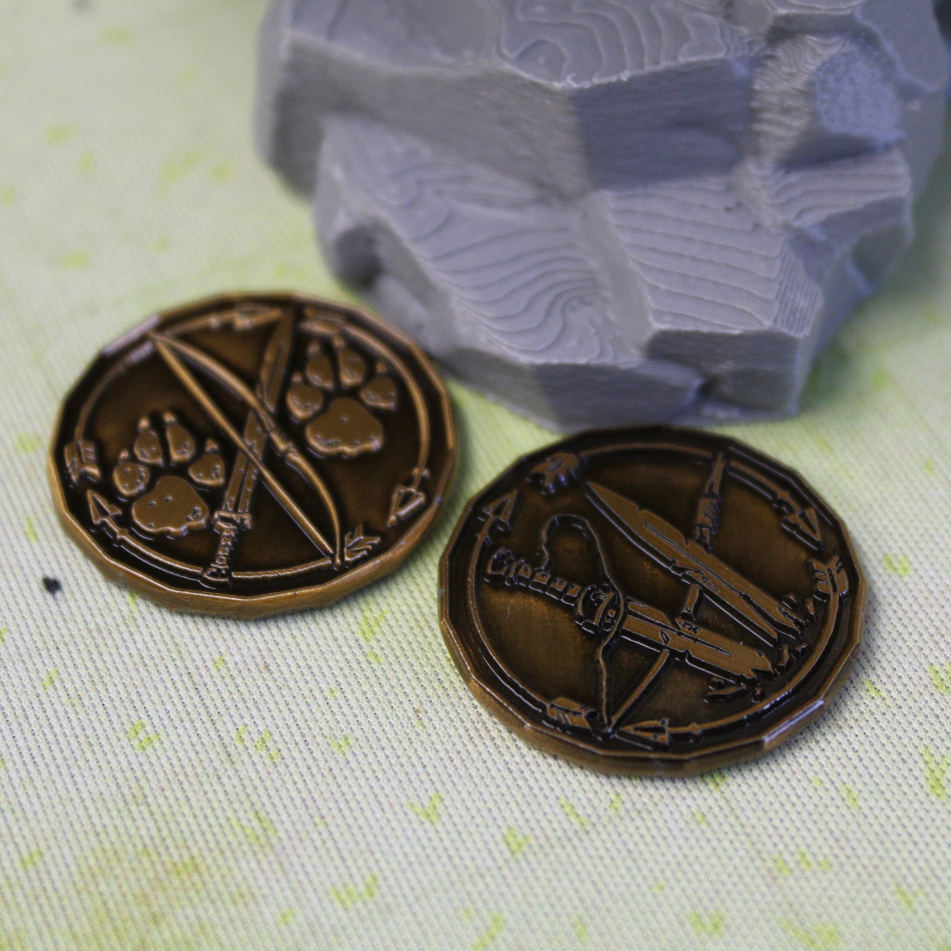 Two golden ranger character tokens sitting on a light green play mat next to a model rock.