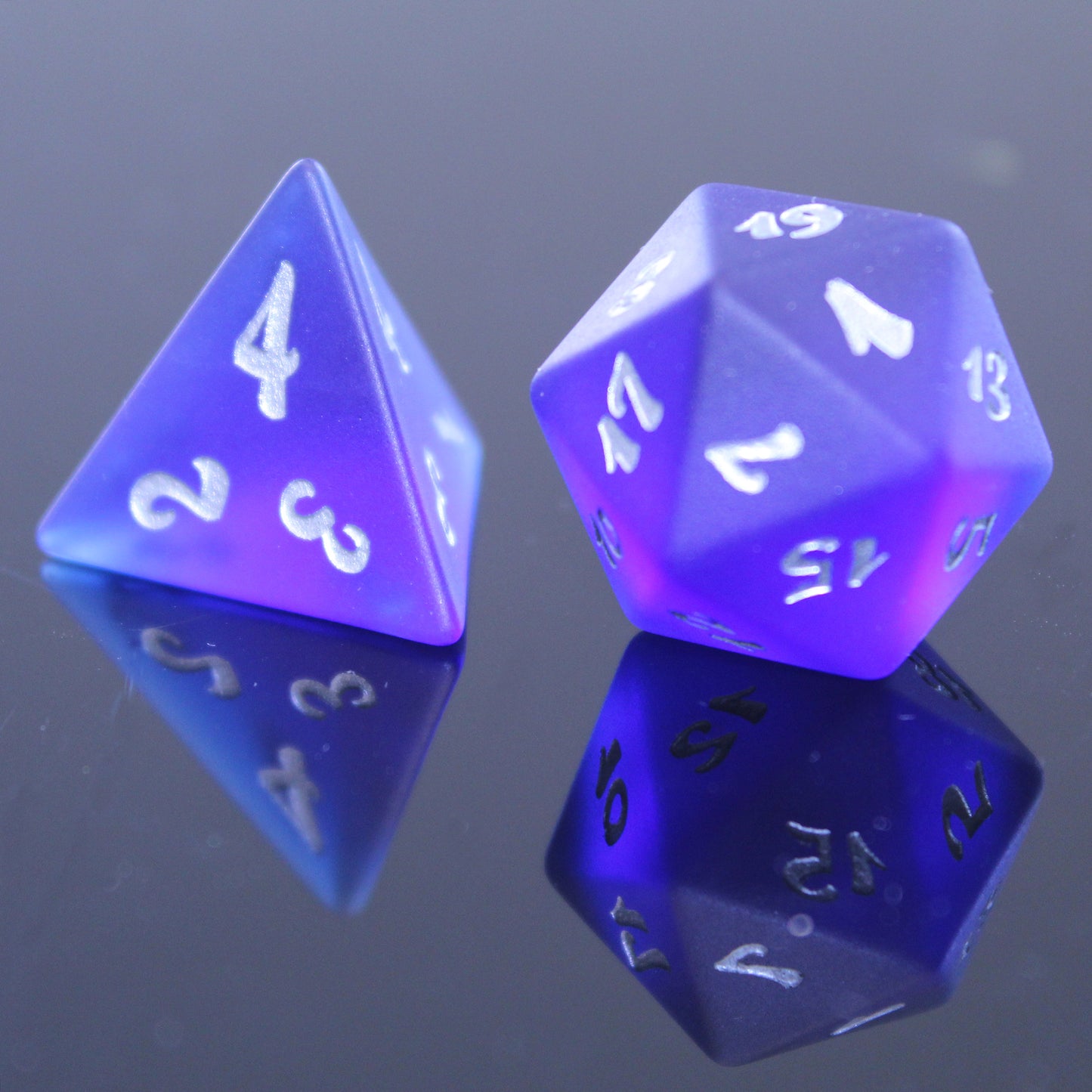 Closeup of two dark blue translucent glass RPG dice with silver numbering on a mirrored surface