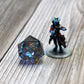 StarGlow Smoke resin dice set placed next to a D&D miniature, with iridescent flashes of color and sharp-edged design for tabletop gameplay.