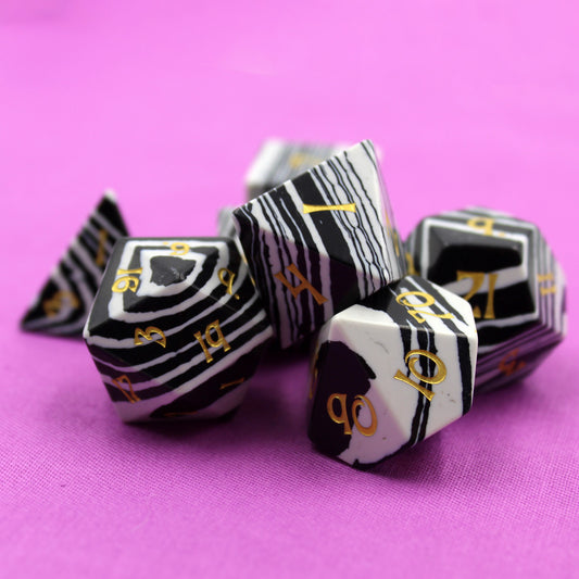 Black and White Striped Dice Set with Gold Lettering on Pink Fabric Background