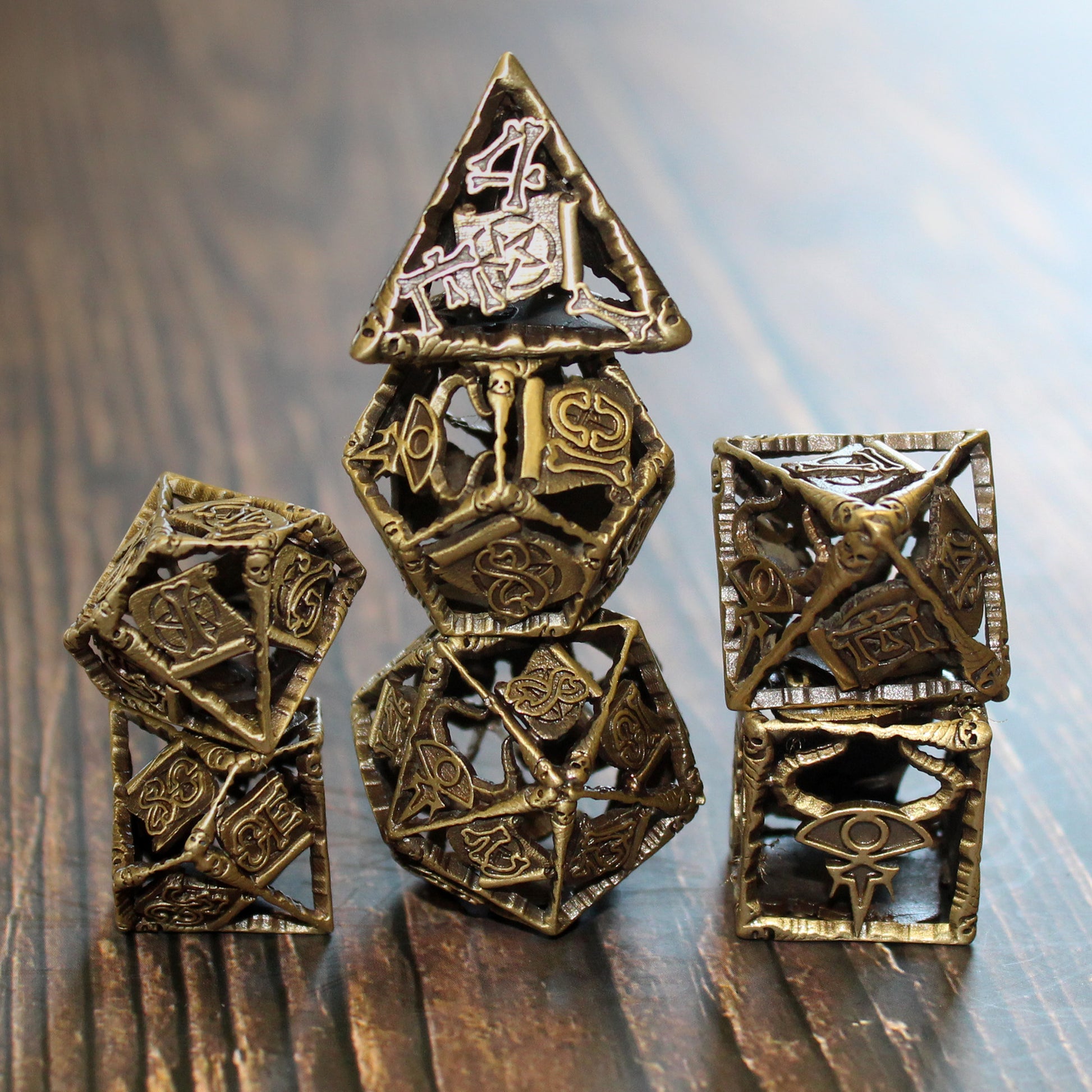 Warlock Cage Dice stacked on a table, showcasing the intricate hollow design and arcane staves framing each face of the electro-plated brass dice.