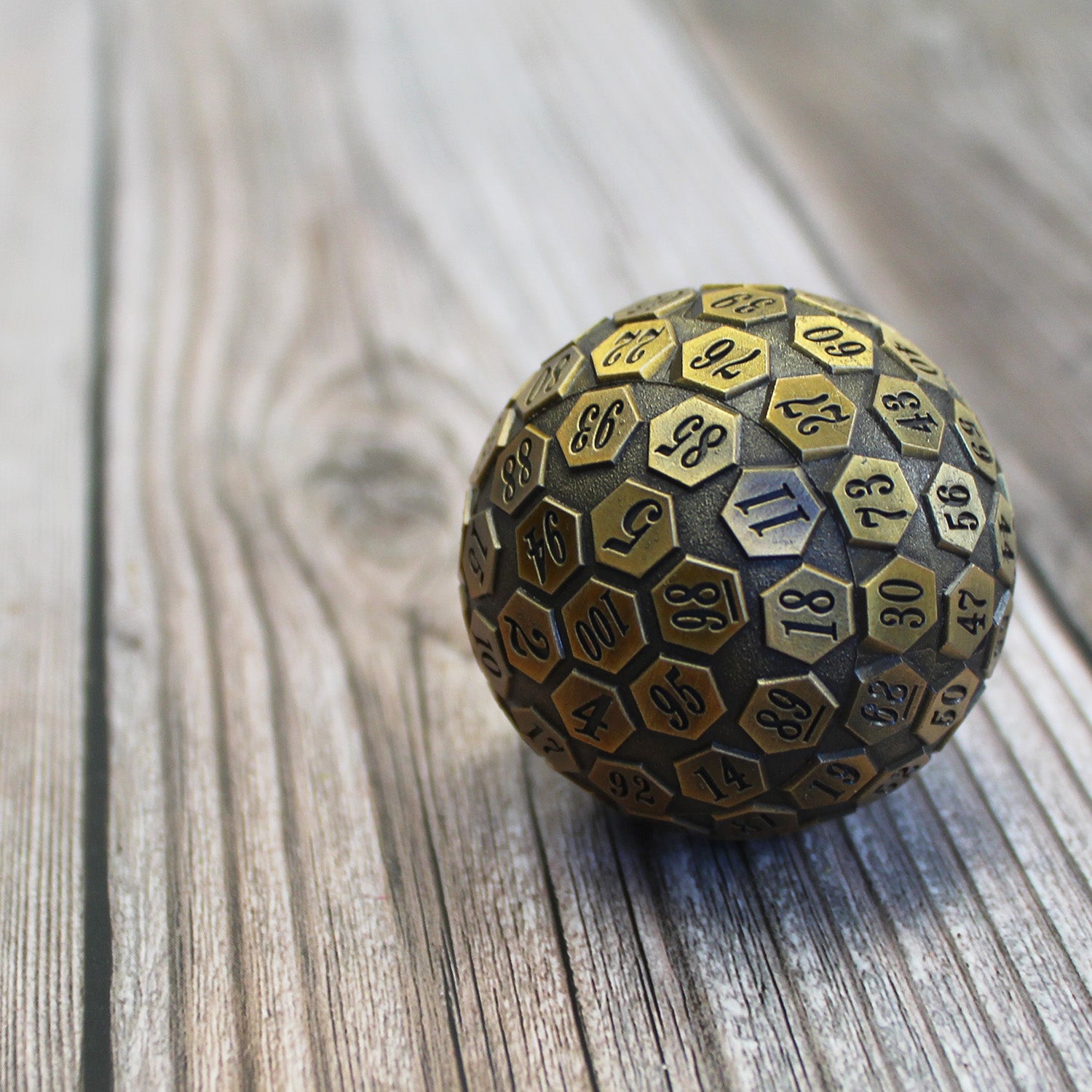 A one hundred sided die cast of a half pound of zinc alloy resting on a wooden surface with the 39 face rolled and the 100 face towards the viewer.